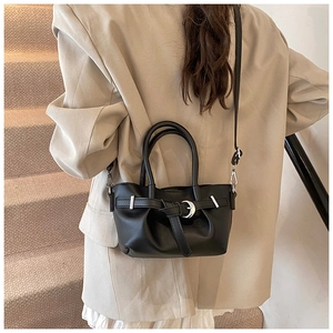 Détail d'un sac seau en cuir noir avec boucle argentée et nœud porté par un mannequin