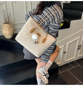 Model wearing a large beige tote bag with brown straps and a cute plush doll charm