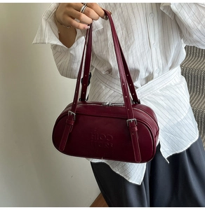 Detailed close-up of dark wine red leather cylinder bag with brand logo and silver metal buckle