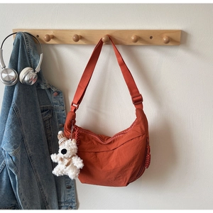 Close-up of orange nylon crescent bag with adjustable strap and cute plush bear charm
