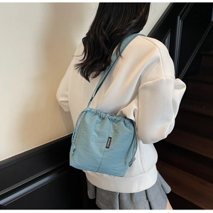 Close-up of light blue drawstring bucket bag with SHUNUO label on casual female model