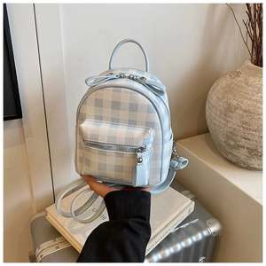 Détail du mini sac à dos à carreaux bleus avec nœuds mignons et fermetures sur une valise