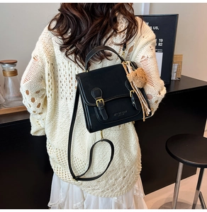 Detail of a black crossbody bag featuring a golden logo and a cute brown bear charm