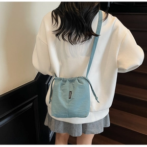 Detail showing the light blue drawstring bucket bag with pleated texture and brand tag