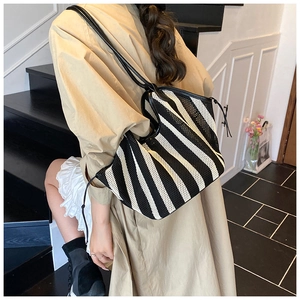 On-shoulder view of large striped woven tote bag with slim black shoulder straps
