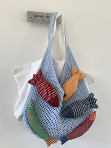 Blue hand-knitted tote bag with five colorful fish-shaped plush toys inside on white wall