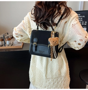 Detail of black vintage leather backpack with dual buckle straps and plush bear charm