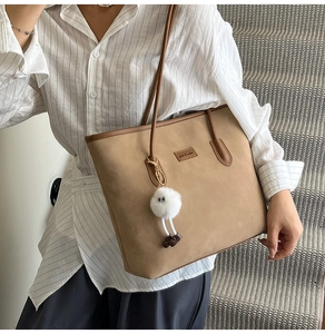 Detail of khaki suede tote bag with plush monster charm and leather brand tag