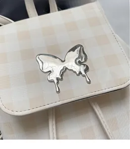 Détail de l'accessoire papillon argenté sur un sac à dos à carreaux beige en similicuir