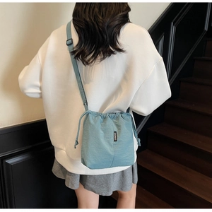 Detail of light blue drawstring bucket bag with black brand label and adjustable strap