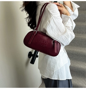 Detail of dark red leather underarm bag with embossed logo and metal buckle strap