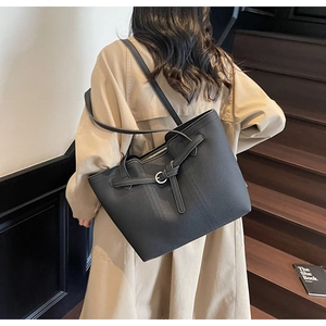 Detailed close-up of large black leather tote bag with silver buckle on beige trench coat