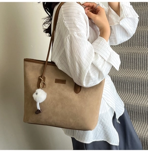 Detail of a brown suede tote bag with leather handles and white plush pom pom charm