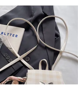 Détail du sac à dos à carreaux crème avec bretelles en cuir et pendentif tissé coloré
