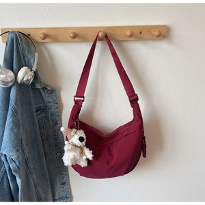 Detail of burgundy crescent dumpling bag with a cute bear charm on a wooden hook