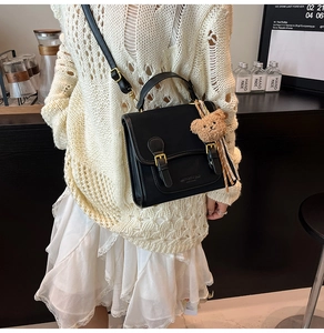 Detail of black leather shoulder bag with a cute plush bear charm and golden pin buckle