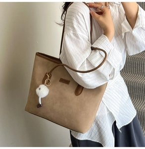 Detail of vintage brown suede tote bag featuring a plush white pompom and brand patch