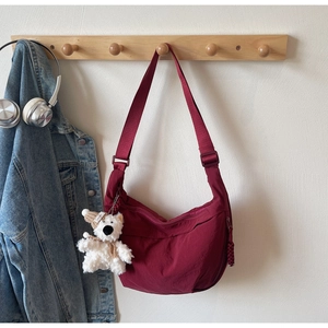 Detail view of burgundy crescent crossbody bag with white plush bear charm on hanger