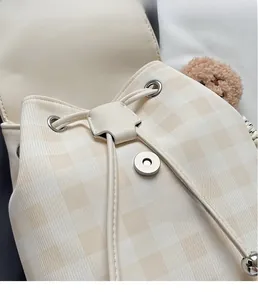 Détail du sac à dos beige à carreaux avec boucle magnétique argentée et breloque en forme d'ours