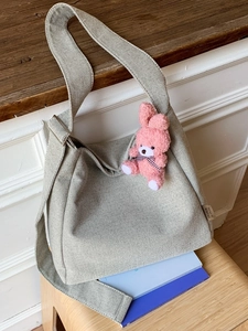 Large beige canvas tote bag with shoulder strap and pink bunny charm on wooden stool