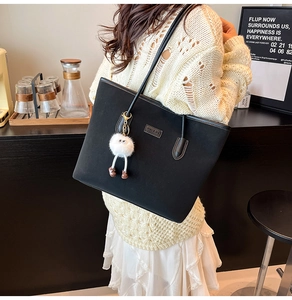 Detail of black suede tote bag with leather straps and cute plush pendant charm