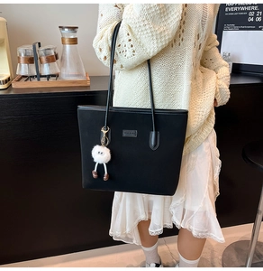 Detail of matte black tote bag with plush charm on stylish cream knit sweater
