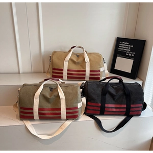 Close-up of canvas travel bags in khaki, olive green, and black with red webbing accents