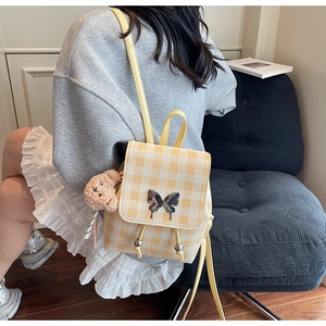 Détail d'un sac à dos à carreaux jaunes avec fermoir papillon argenté et petit ours