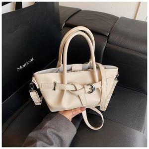 Détail du sac seau beige avec boucle décorative et bandoulière sur un canapé en cuir noir