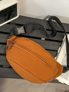 Bright orange nylon crossbody chest bag with adjustable strap on a modern urban background