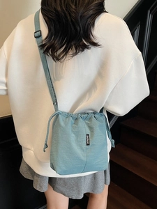 Minimalist blue drawstring bucket bag shown worn crossbody by a model in casual style