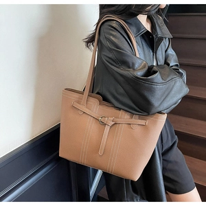 Close-up of tan pebble leather tote with white contrast stitching and gold buckle detail