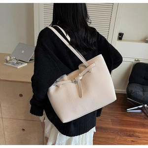 Detail of beige lychee leather tote bag with decorative buckle on model shoulder