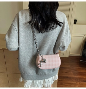 Pink checkered crossbody bag with silver chain strap and balloon dog charm on a model