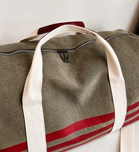 Detail view of large army green canvas travel bag with red stripes and reinforced handles
