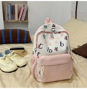 Zaino scolastico rosa e beige con stampe di lettere in un ambiente domestico