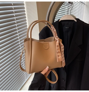 Detail of camel lychee leather bucket bag with fashion logo and plaid silk scarf