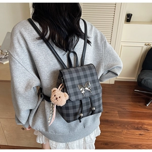 Détail du sac à dos à carreaux gris avec boucle papillon argentée et pendentif ours peluche