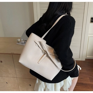 Close-up of a large beige leather tote bag featuring crisscross strap and gold ring detail