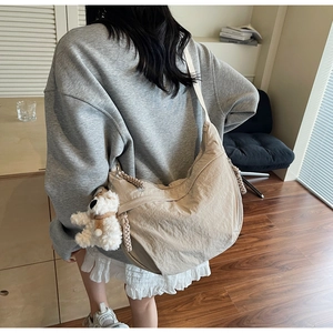 Close-up of beige crescent bag with woven zipper pull and cute plush bear charm accessory