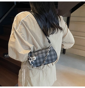 Detail of grey plaid underarm bag with silver chain and rabbit charm on a model
