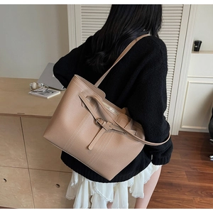 Brown lychee grain tote bag with decorative belt buckle shown on shoulder of a model