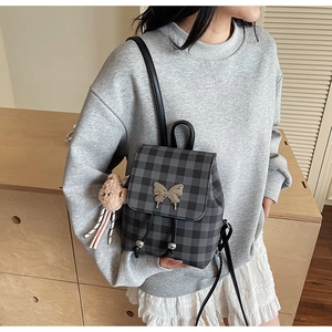 Gros plan du mini sac à dos à carreaux noir et gris avec boucle papillon dorée et breloque