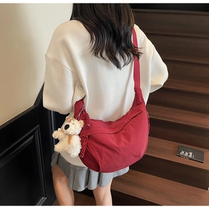 Detail of burgundy crescent crossbody bag with plush bear charm worn by a model