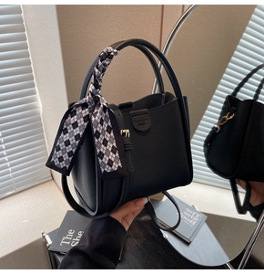 Detail of black litchi leather handbag with checkerboard scarf handle and gold buckle