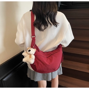 Rear view of model wearing a red nylon crescent crossbody bag with a plush bear charm