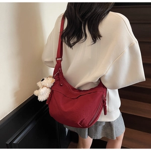 Detail of red nylon crescent bag with a white plush dog charm on a wooden staircase