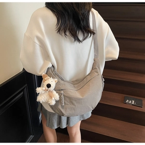 Close-up of grey dumpling bag with a plush bear charm on a wood staircase