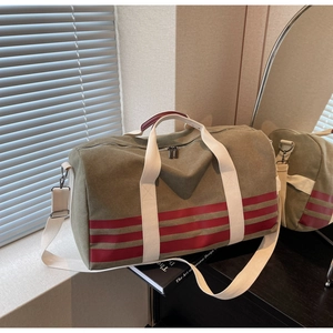 Detail of army green travel bag with red stripes and white canvas handles on wooden table