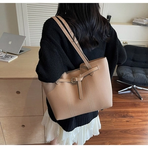 Detail of large beige tote bag with buckle decoration shown on shoulder for daily commute